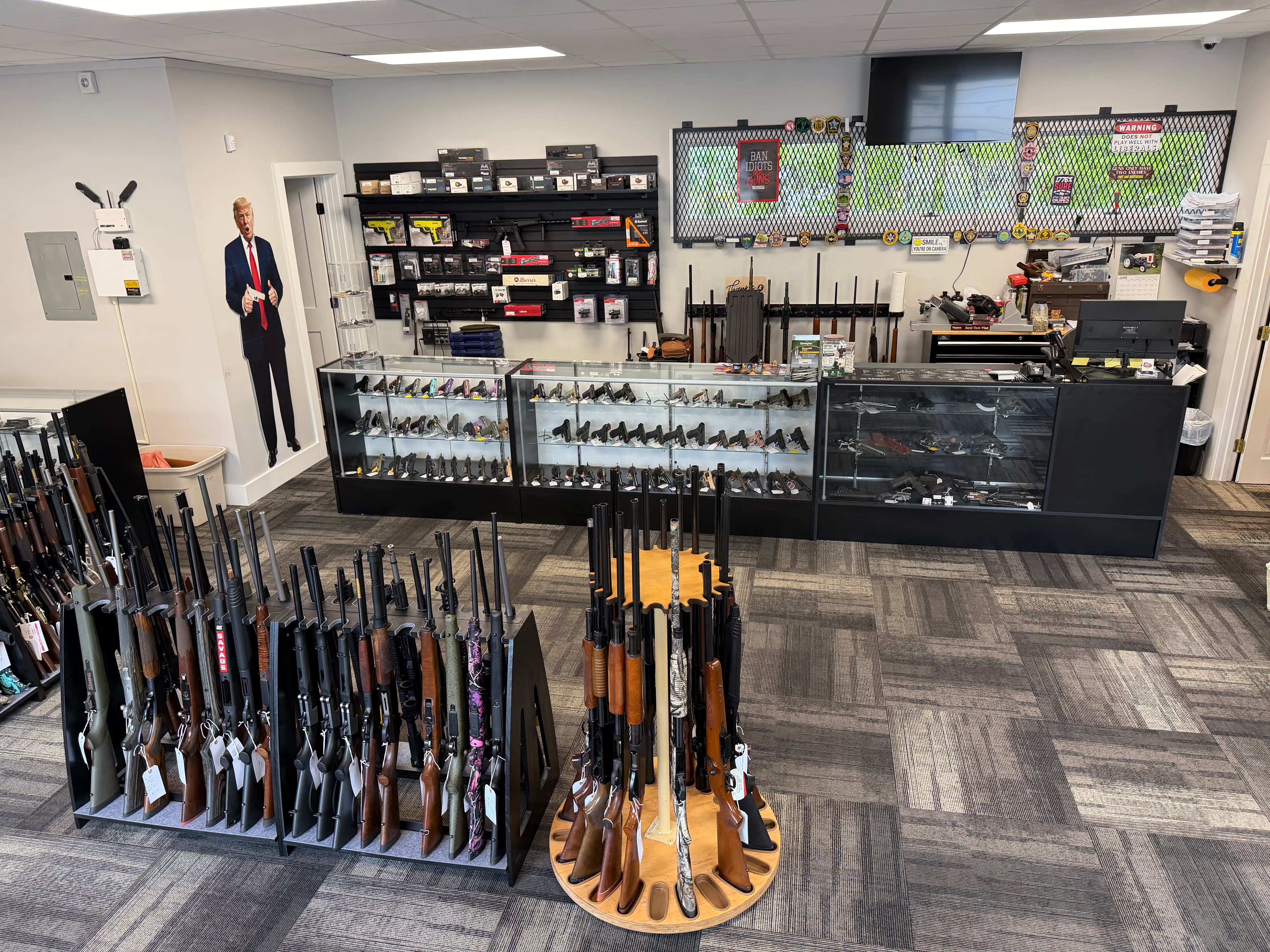 Gun shop interior with rifles on racks, handguns in glass cases, and a Trump cutout.