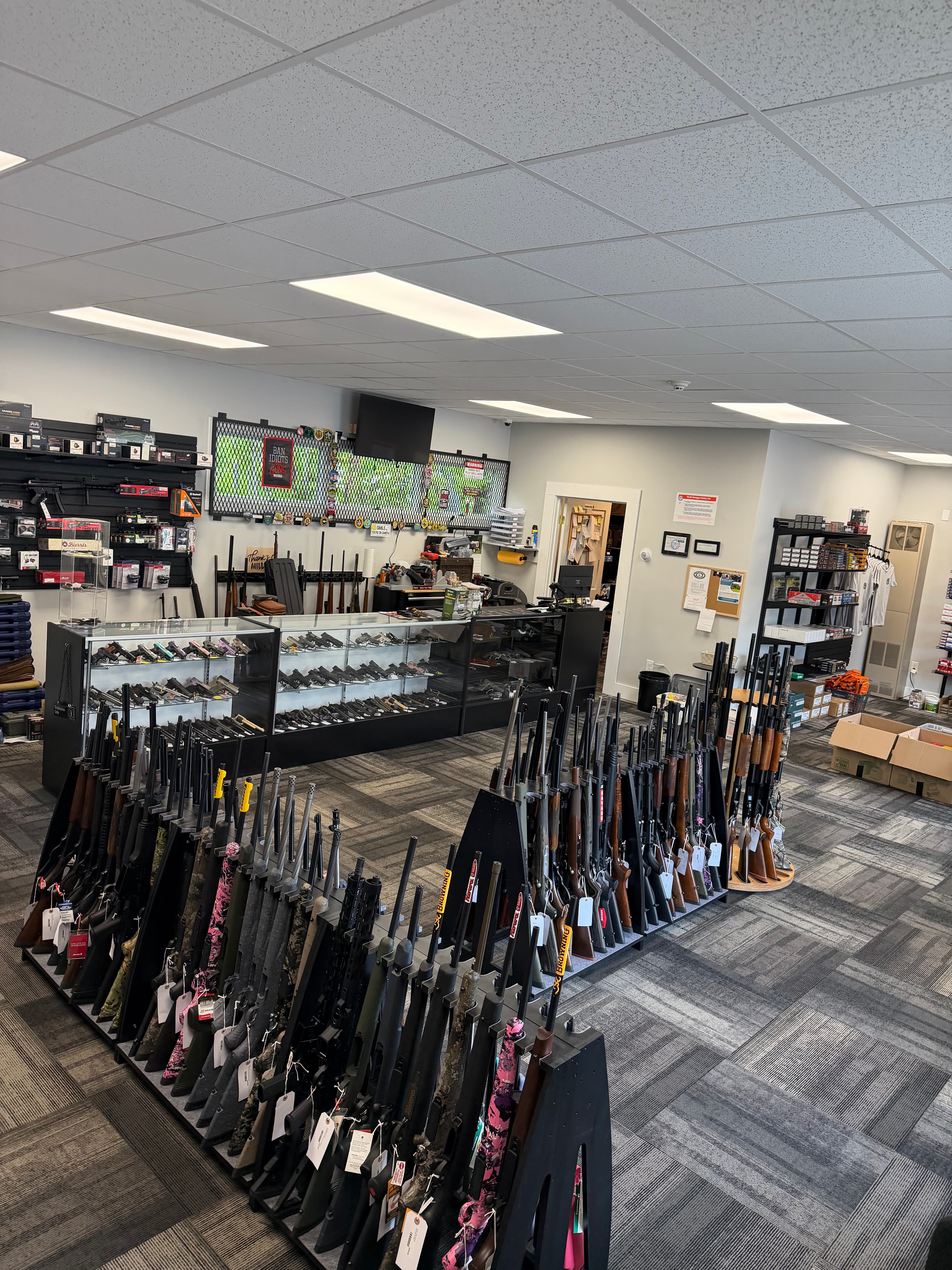Gun shop interior with rifles on floor racks and handguns displayed in glass cases.