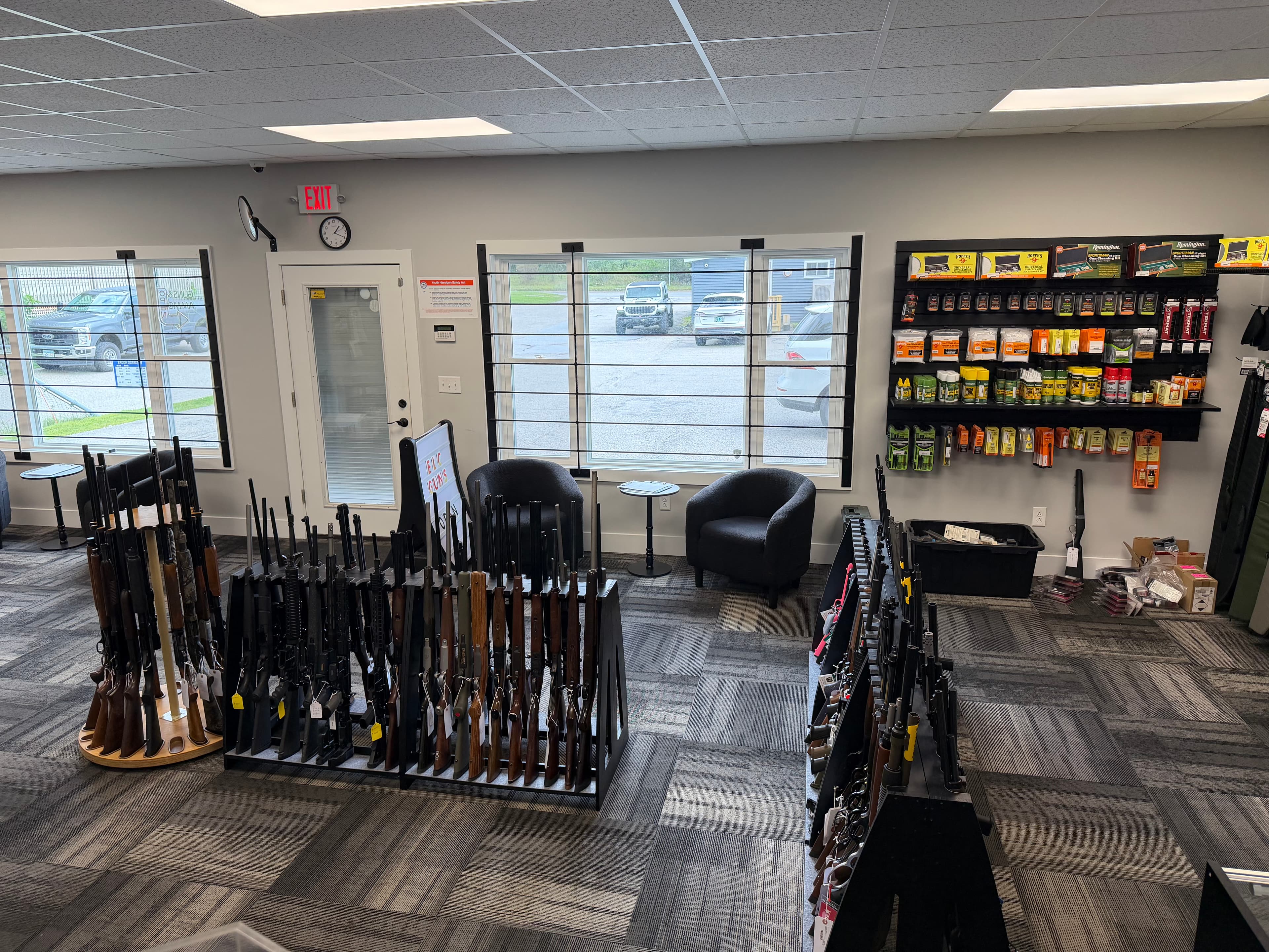 Gun shop interior with rifles on display racks, shelves of accessories, and two armchairs.